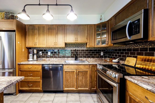 Kitchen featuring light tile patterned floors, a sink, decorative backsplash, stainless steel appliances, and glass insert cabinets | Image 6