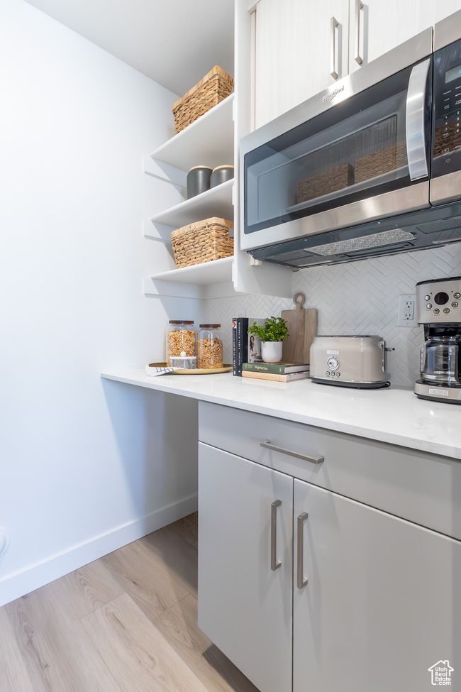 Kitchen featuring stainless steel microwave, open shelves, backsplash, light countertops, and light wood-style floors | Image 12