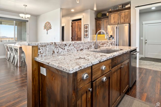 Kitchen featuring light stone counters, dark wood-style flooring, a sink, stainless steel appliances, and a center island with sink | Image 13