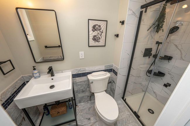Bathroom with tile walls, sink, a shower with door, and toilet | Image 19