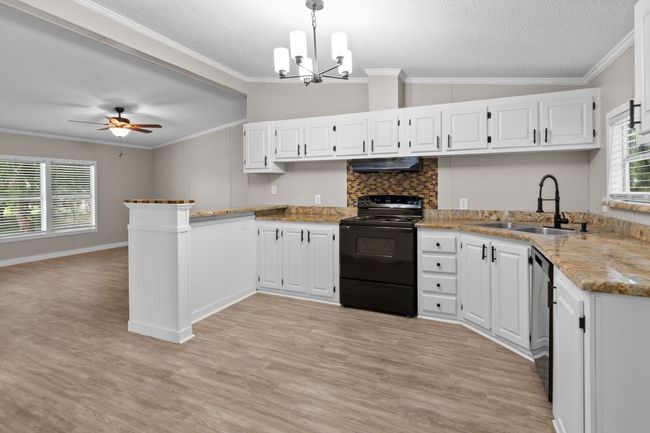 Kitchen with black / electric stove, under cabinet range hood, a peninsula, light wood finished floors, and ornamental molding | Image 19