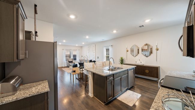 Kitchen with stainless steel appliances, dark brown cabinets, dark wood-style flooring, a kitchen island with sink, and light stone countertops | Image 8