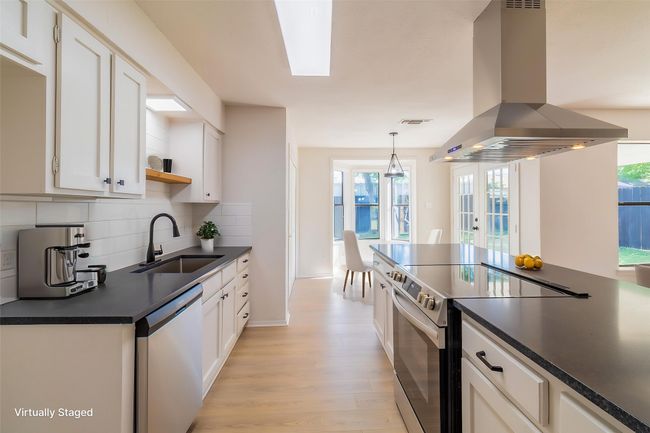 Kitchen with dark countertops, a sink, island range hood, stainless steel electric range oven, and dishwasher | Image 4