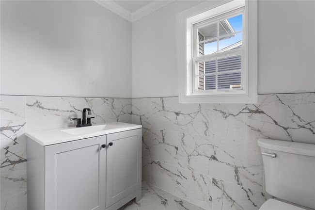 Half bath with tile walls, toilet, crown molding, marble finish flooring, and vanity | Image 5