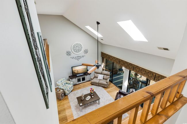 Living room with vaulted ceiling with skylight, wood finished floors, a fireplace, and visible vents | Image 20