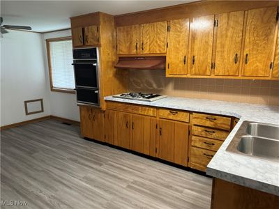 Kitchen with white gas cooktop, decorative backsplash, light hardwood / wood-style flooring, oven, and ceiling fan | Image 3