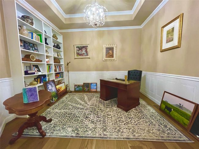 Office area featuring a chandelier, wood finished floors, a wainscoted wall, a raised ceiling, and crown molding | Image 9