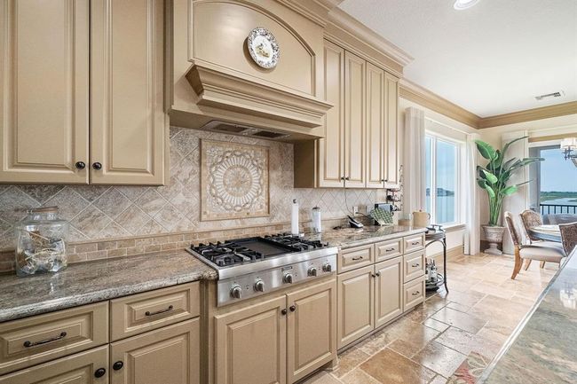 The gourmet kitchen showcases a gas cooktop, granite counters, and a mosaic backsplash | Image 14