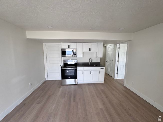 Kitchen with a sink, appliances with stainless steel finishes, dark countertops, baseboards, and wood finished floors | Image 29