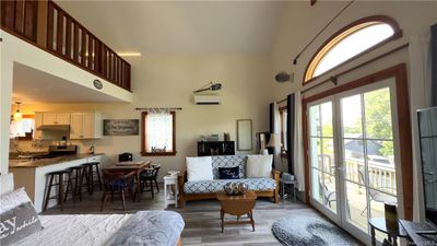 Living room featuring high vaulted ceiling, a wall mounted AC, and wood-style floors, slider to front deck | Image 3