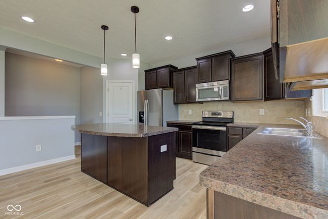 kitchen featuring stainless steel appliances, light wood-style flooring, dark brown cabinetry, a center island, and backsplash | Image 6