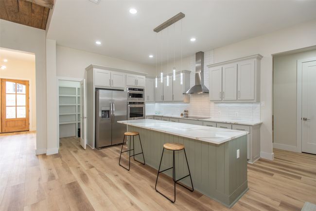 Kitchen featuring a center island, hanging light fixtures, wall chimney range hood, backsplash, and appliances with stainless steel finishes | Image 5