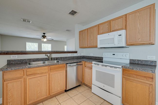 Kitchen with white appliances, a ceiling fan, dark countertops, and light tile patterned flooring | Image 8