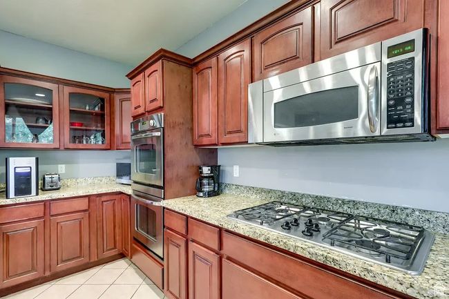 Kitchen with light tile patterned flooring, glass insert cabinets, light stone counters, and stainless steel appliances | Image 6