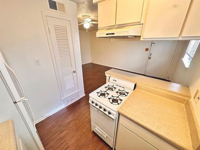 Kitchen featuring white appliances, under cabinet range hood, dark wood-style floors, ceiling fan, and baseboards | Image 6