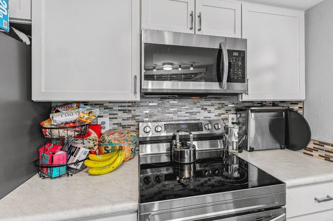 Kitchen with stainless steel appliances, decorative backsplash, light countertops, and white cabinetry | Image 11