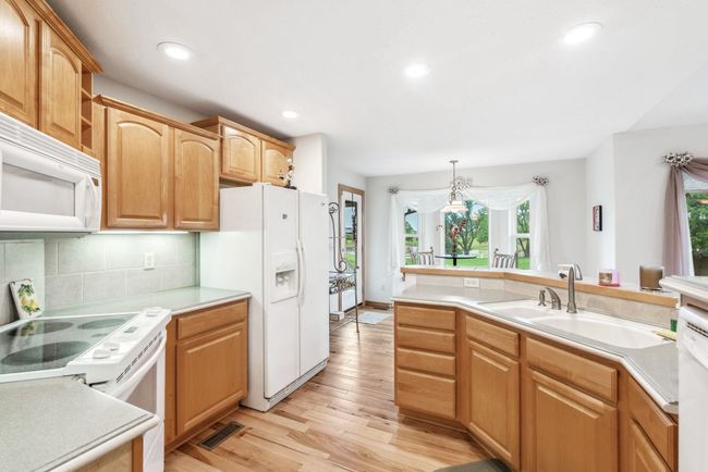 Kitchen featuring white appliances, a sink, light wood finished floors, tasteful backsplash, and light countertops | Image 7