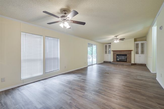 Unfurnished living room featuring a ceiling fan, a textured ceiling, dark wood finished floors, a fireplace, and baseboards | Image 7
