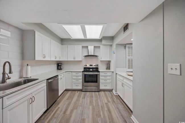 Kitchen with wall chimney range hood, appliances with stainless steel finishes, a sink, light wood-type flooring, and white cabinetry | Image 13