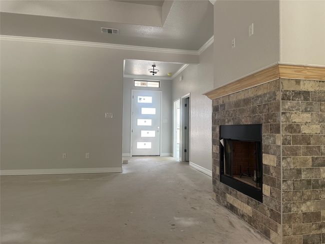 Unfurnished living room with concrete floors, crown molding, visible vents, and a fireplace | Image 20