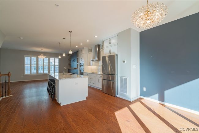 Kitchen featuring stainless steel appliances, white cabinets, a chandelier, a center island with sink, and dark hardwood / wood-style floors | Image 6