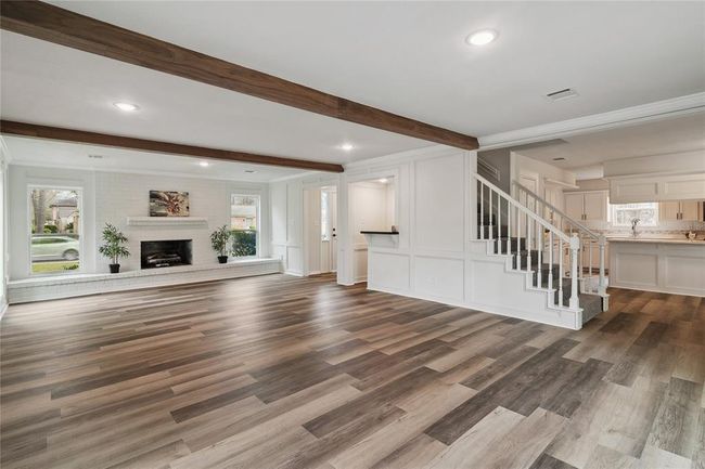 The distinguished open layout flows seamlessly into the modern kitchen, and a stylish staircase leads to the upper level. This spacious living area with the cozy brick fireplace and ample natural light from large windows is an enchanting space to spend time together on a relaxing day. | Image 9