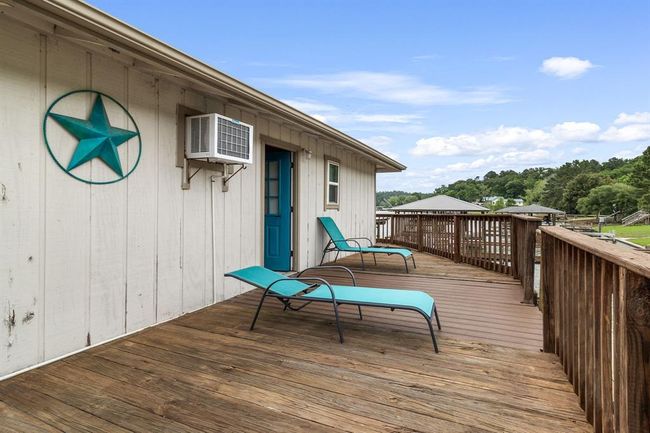 This photo showcases a rustic wooden deck with two turquoise lounge chairs, offering a serene view of the surrounding greenery and water. The exterior features a charming wood-paneled wall with a decorative star and a vibrant blue door, perfect for relaxation and enjoying the outdoors. | Image 35