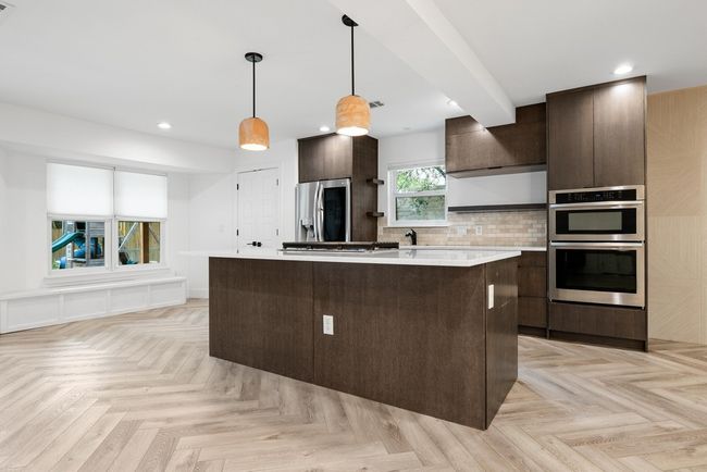 Kitchen with stainless steel appliances, a center island, dark brown cabinets, backsplash, and light countertops | Image 12