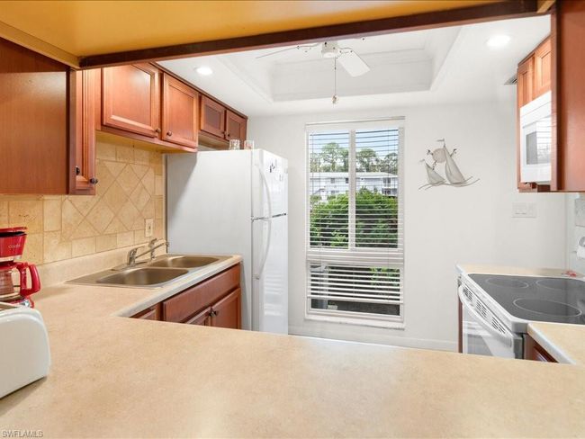 Kitchen with tasteful backsplash, white appliances, a ceiling fan, a raised ceiling, and a sink | Image 24