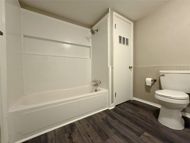 Full bath featuring toilet, wood finished floors, washtub / shower combination, a textured ceiling, and wainscoting | Image 10