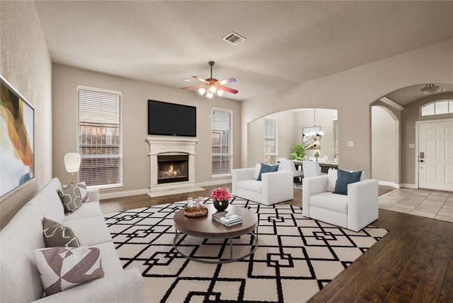 Living room featuring arched walkways, wood finished floors, a warm lit fireplace, a ceiling fan, and baseboards | Image 4