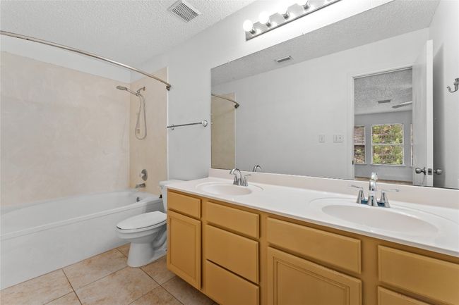 Full bath with a textured ceiling, toilet, shower / bath combination, tile patterned flooring, and double vanity | Image 25