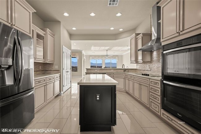 Kitchen with wall chimney exhaust hood, a peninsula, visible vents, black appliances, and decorative backsplash | Image 13