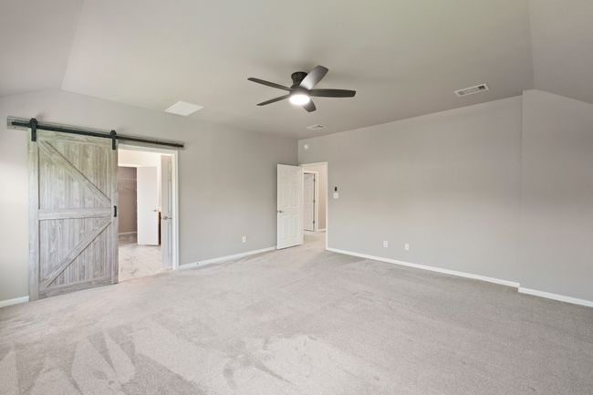 Unfurnished bedroom featuring lofted ceiling, a barn door, light colored carpet, baseboards, and ceiling fan | Image 17