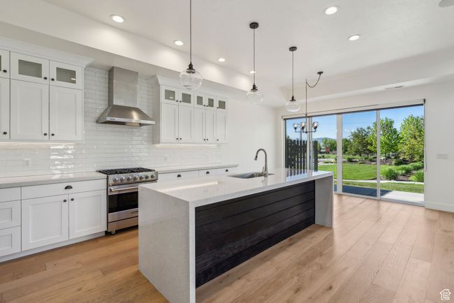 Kitchen featuring high end stainless steel range, wall chimney exhaust hood, a sink, tasteful backsplash, and light wood-style floors | Image 17