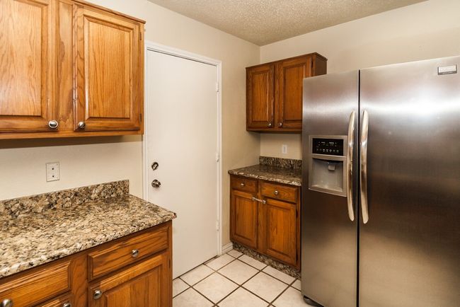 Kitchen featuring stainless steel fridge, brown cabinets, light stone countertops, light tile patterned floors, and a textured ceiling | Image 9