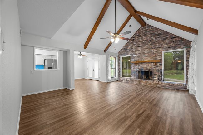 Unfurnished living room with ceiling fan, baseboards, high vaulted ceiling, wood finished floors, and a brick fireplace | Image 8