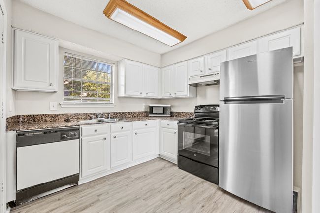 Kitchen with under cabinet range hood, white cabinets, light wood-type flooring, and appliances with stainless steel finishes | Image 5