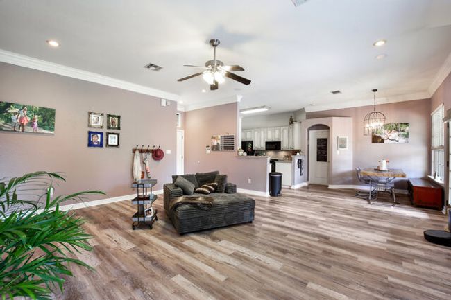 Living room with a ceiling fan, light wood-style flooring, a chandelier, ornamental molding, and arched walkways | Image 6