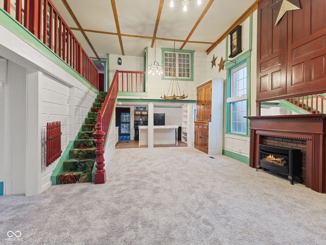 unfurnished living room featuring a lit fireplace, stairway, a high ceiling, carpet, and an inviting chandelier | Image 4