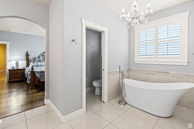 Bathroom with a bathing tub, an inviting chandelier, toilet, tile walls, and hardwood / wood-style flooring | Image 50