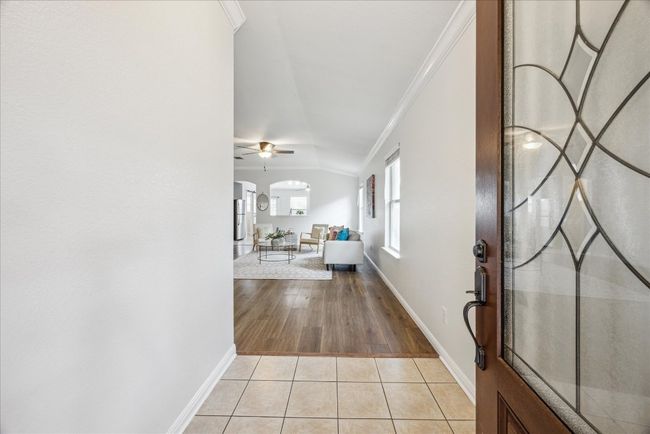 Entrance foyer featuring stylish front door, crown molding, light tile floors, arched walkways, and vaulted ceiling | Image 6