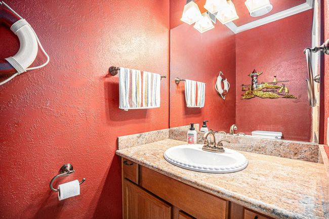 Conveniently located off of the living room, the half-bath features a stylish vanity with a granite countertop and a decorative mirror. The walls are painted in a vibrant color, complemented by nautical-themed accents. | Image 15