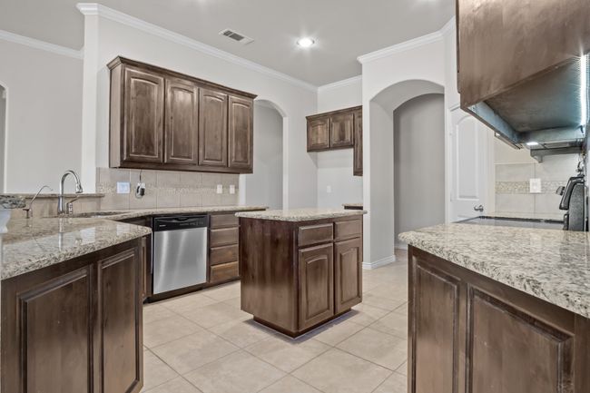 Kitchen featuring crown molding, a sink, dishwasher, arched walkways, and visible vents | Image 6
