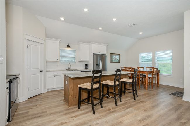 Kitchen featuring lofted ceiling, a kitchen island, stainless steel appliances, a kitchen bar, and white cabinets | Image 14