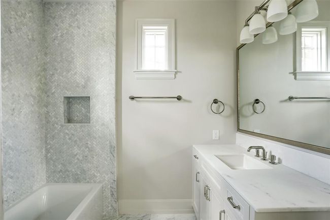 Designed with sophistication, this en-suite bath showcases a striking tub and shower combo accented by a gorgeous tile surround and Farmhouse Stone Carrara marble flooring. A sleek vanity, topped with White Noble Marble, is complemented by custom cabinetry, blending style and functionality seamlessly. | Image 23
