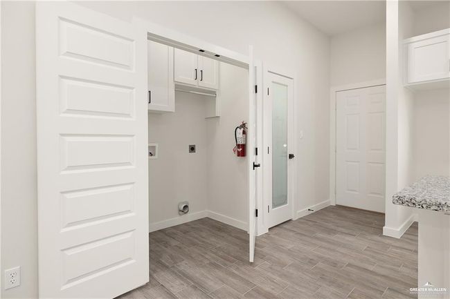 Laundry room with hookup for an electric dryer, cabinet space, hookup for a washing machine, and light wood-style flooring | Image 10