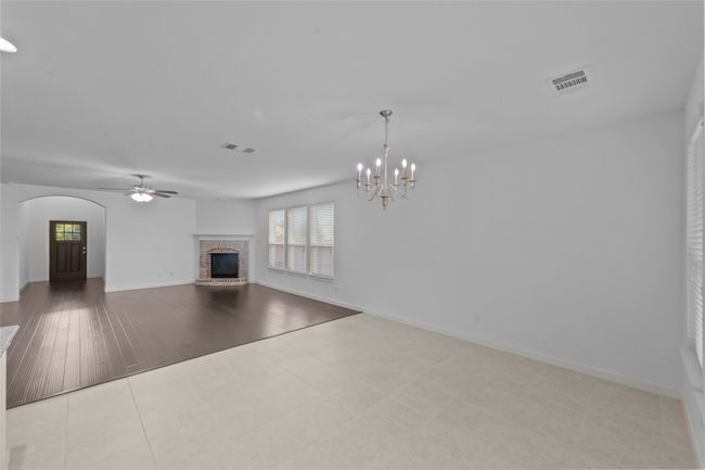 Unfurnished living room featuring a brick fireplace, arched walkways, ceiling fan, and a chandelier | Image 17