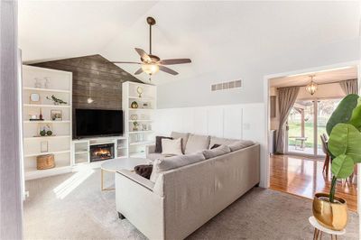 Living room featuring built in shelves, wood walls, light hardwood / wood-style floors, lofted ceiling, and ceiling fan with notable chandelier | Image 3