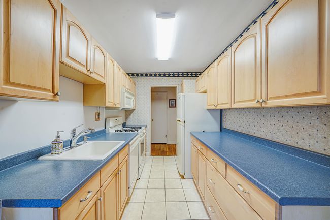 Kitchen featuring white appliances, a sink, light brown cabinetry, light tile patterned floors, and dark countertops | Image 5
